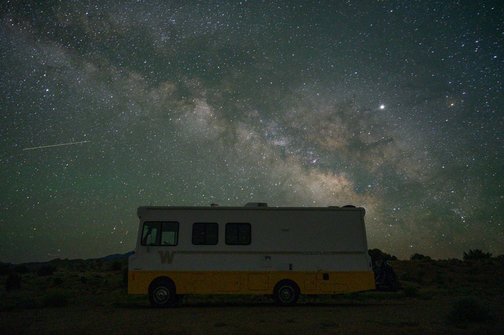 A white and yellow RV on a hill with the milky way shown on the sky